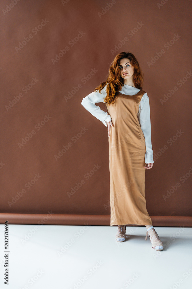 Beautiful young girl in beige dress posing on brown background