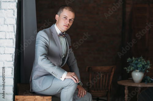 A guy in business clothes with accessories and cufflinks. Portrait of a man dressed in a classic jacket, white shirt and a bow tie. Preparing the bridegroom for the wedding day. © romannoru