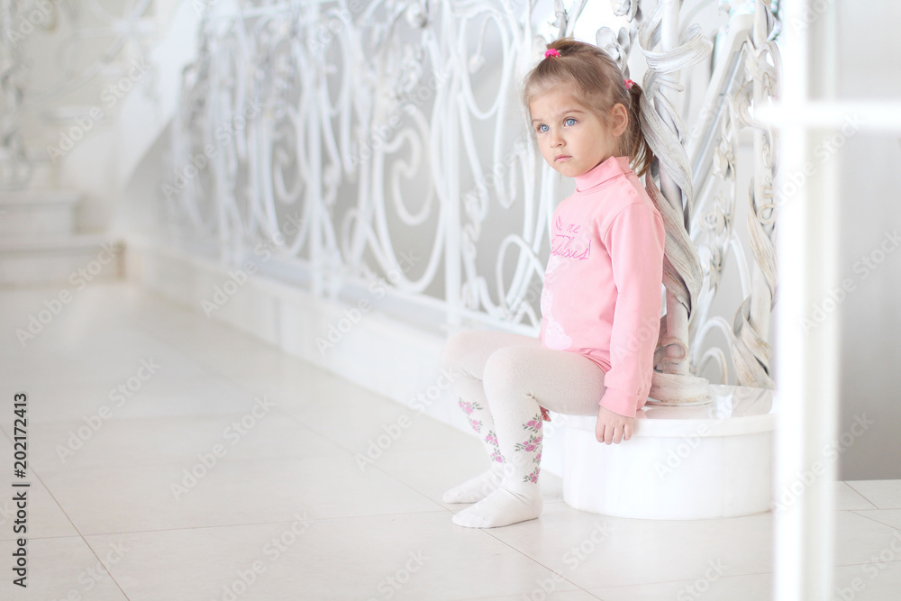 Pensive little girl sitting on the stairs. Bright interior in the house. Pensive little girl sitting on the stairs. Bright interior in the house.