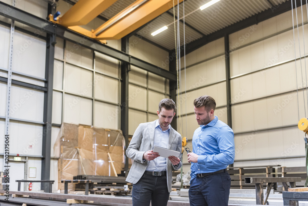 Two businessmen sharing tablet on factory shop floor Two businessmen sharing tablet on factory shop floor