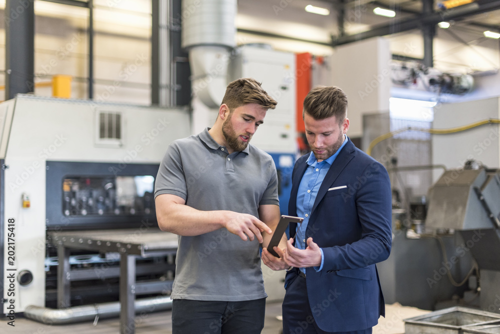 Employee explaining workpiece to businessman on factory shop floor Employee explaining workpiece to businessman on factory shop floor