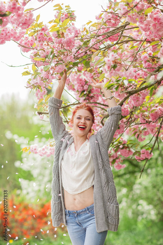 Beautiful young woman with red hair having fun standing in cherry blossom tree, springtime garden mood