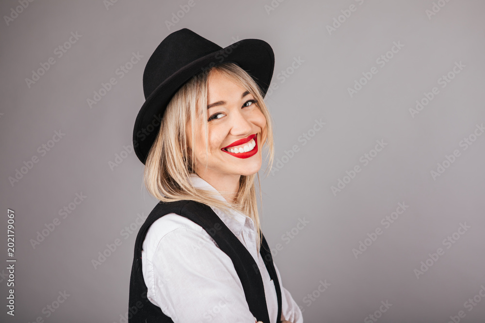 Lovely elegant hipster style young woman in hat on grey background. Smiling beauty Lovely elegant hipster style young woman in hat on grey background. Smiling beauty