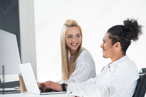 young multiethnic colleagues smiling each other while working together in office