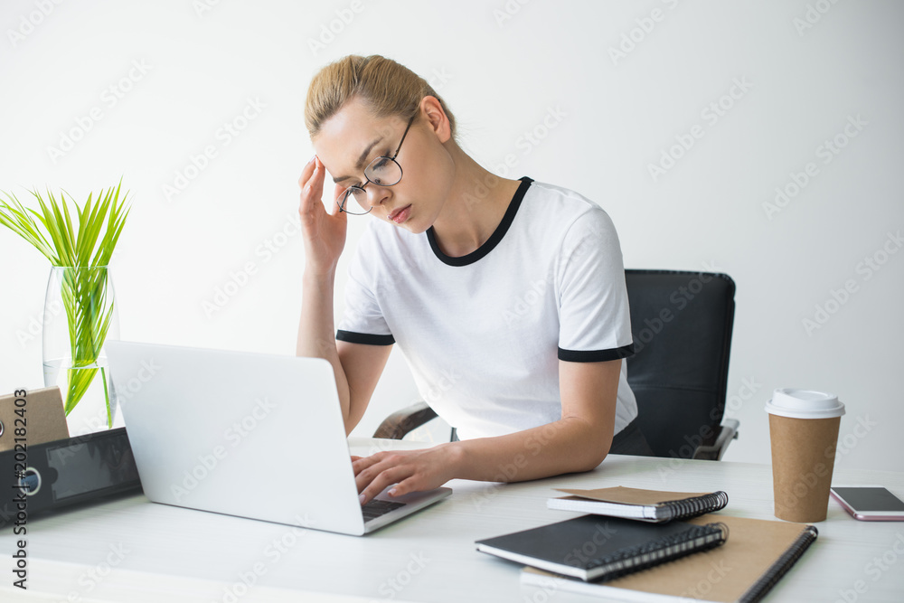 tired young businesswoman in eyeglasses using laptop in office tired young businesswoman in eyeglasses using laptop in office