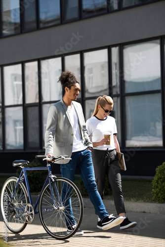 Fototapeta Naklejka Na Ścianę i Meble -  smiling young multiethnic couple with bicycle walking on street