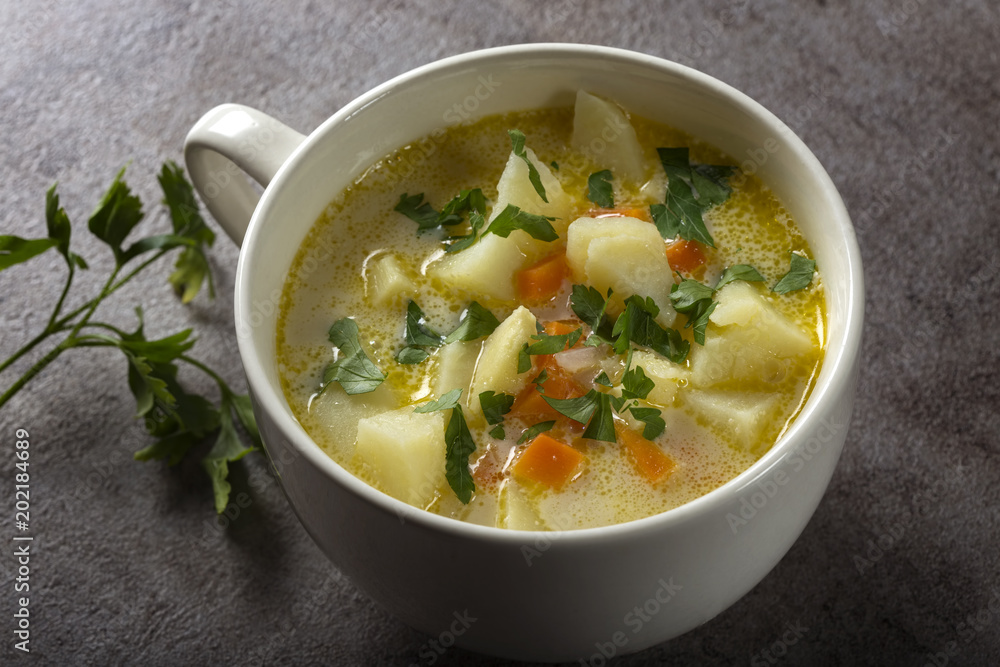 Healthy soup in white bowl with carrot, potatoes and parsley