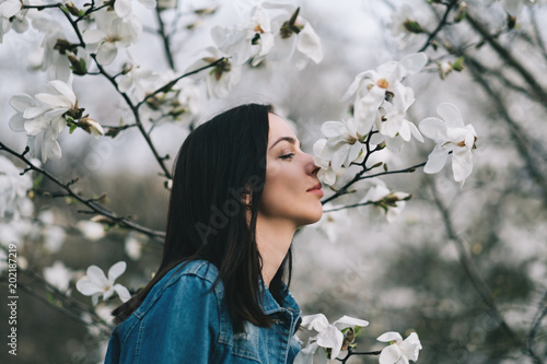 Young attractive slim woman wearing blue stylish jeans jacket posing over blossoming magnolia trees