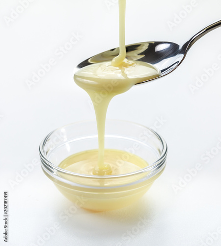 closeup pouring condensed milk with teaspoon on white background photo