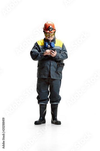 The studio shot of serious senior bearded male miner standing at the camera with smartphone on a white background. © master1305