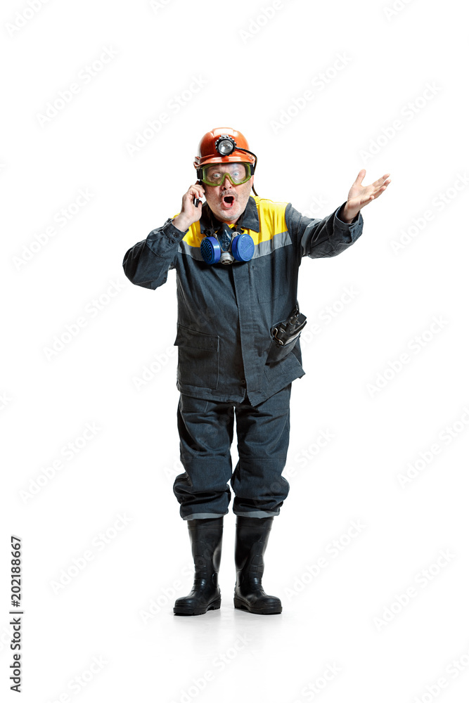 The studio shot of surprised senior bearded male miner standing at the camera with smartphone on a white background. The studio shot of surprised senior bearded male miner standing at the camera with smartphone on a white background.