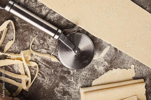 Raw dough and wheel cutter on kitchen table photo