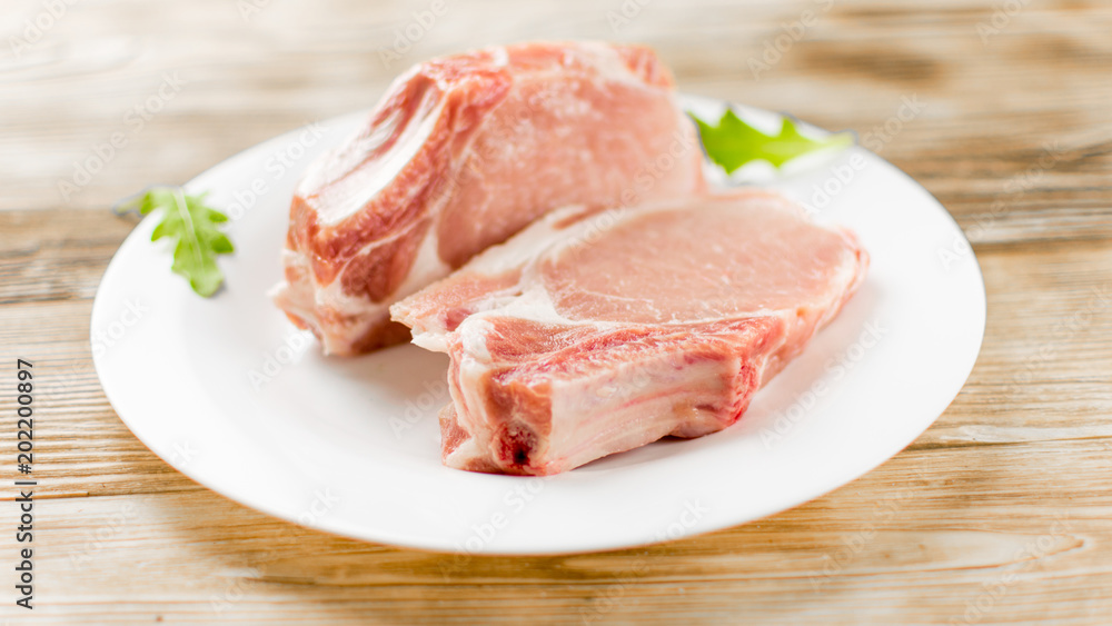 Raw pork brisket, ribs on a white plate on a wooden background.