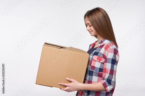 Delivery, relocation and unpacking. Side view portrait of woman holding cardboard box looking at box, isolated