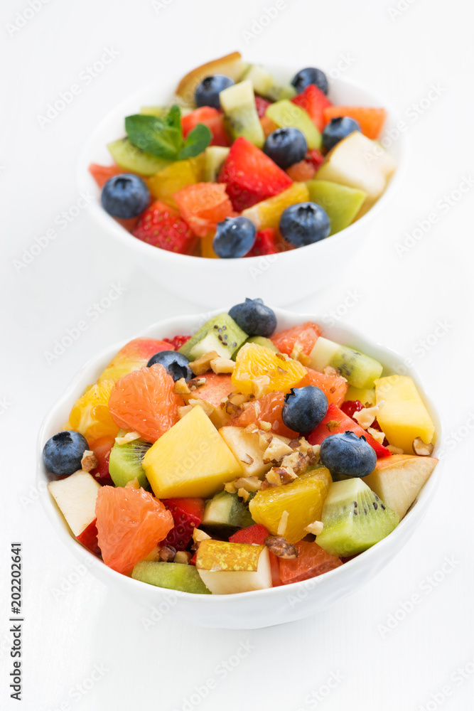 two bowls of fruit salad on white table, vertical