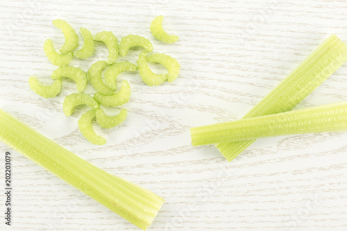 Three green celery sticks with fresh chopped pieces isolated on light wooden background. photo