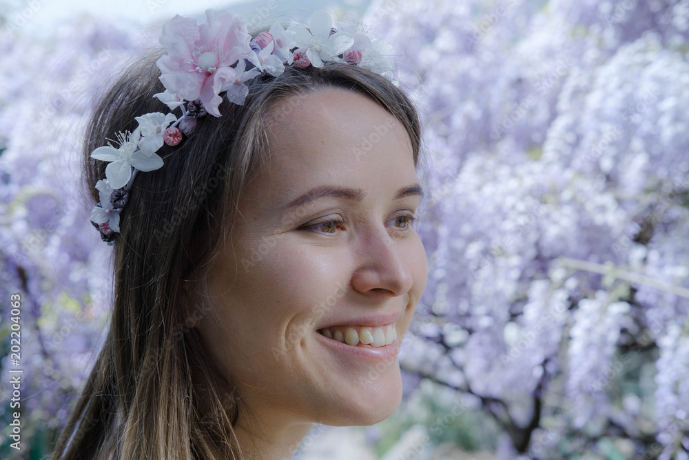 Obraz premium Young blonde curly hair woman in blooming wisteria garden in spring. Woman wearing in lilac dress