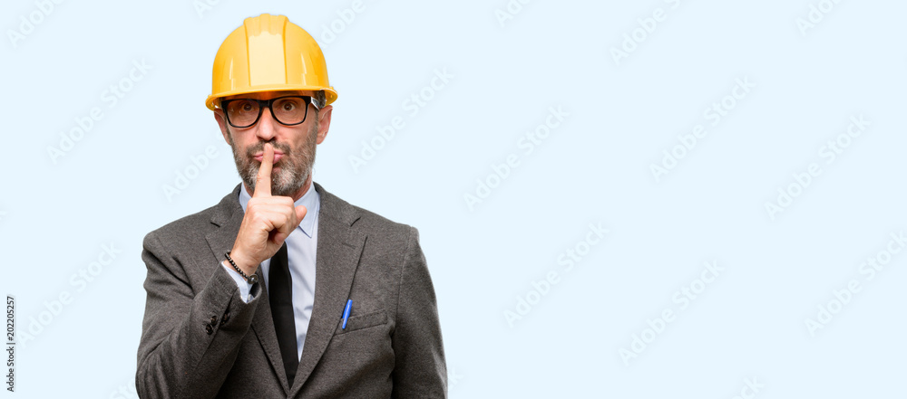 Senior architect or engineer with index finger on lips, ask to be quiet. Silence and secret concept isolated over blue background Senior architect or engineer with index finger on lips, ask to be quiet. Silence and secret concept isolated over blue background
