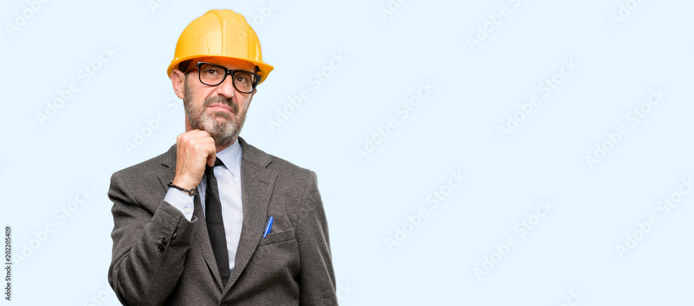 Senior architect or engineer thinking and looking up expressing doubt and wonder isolated over blue background