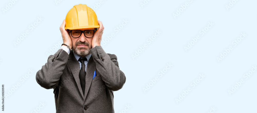 Senior architect or engineer covering ears ignoring annoying loud noise, plugs ears to avoid hearing sound. Noisy music is a problem. isolated over blue background Senior architect or engineer covering ears ignoring annoying loud noise, plugs ears to avoid hearing sound. Noisy music is a problem. isolated over blue background