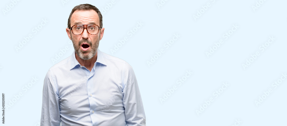 Middle age man with glasses scared in shock, expressing panic and fear isolated over blue background Middle age man with glasses scared in shock, expressing panic and fear isolated over blue background