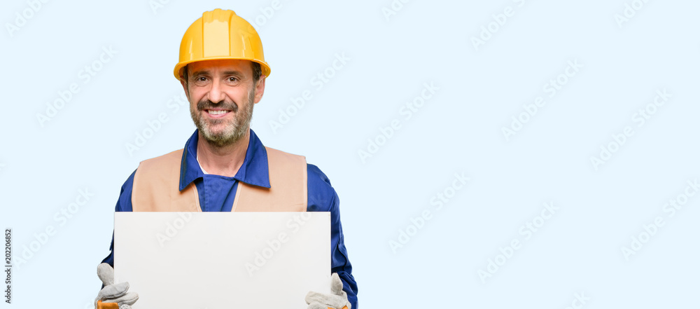 Senior engineer man, construction worker holding blank advertising banner, good poster for ad, offer or announcement, big paper billboard isolated over blue background Senior engineer man, construction worker holding blank advertising banner, good poster for ad, offer or announcement, big paper billboard isolated over blue background
