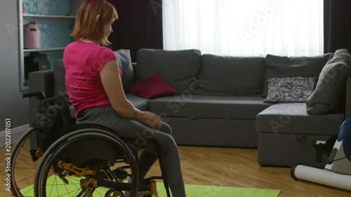 Medium shot of independent paraplegic woman getting out of wheelchair and sitting down on yoga mat