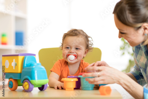 Billede på lærred Curly baby boy and woman playing with toys in daycare or kindergarten