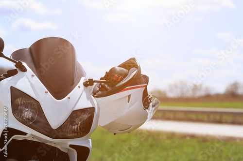 Closeup of a racing white motorcycle on an empty road in the background with a helmet on the steering wheel on a sunny day. The view over the handlebars
