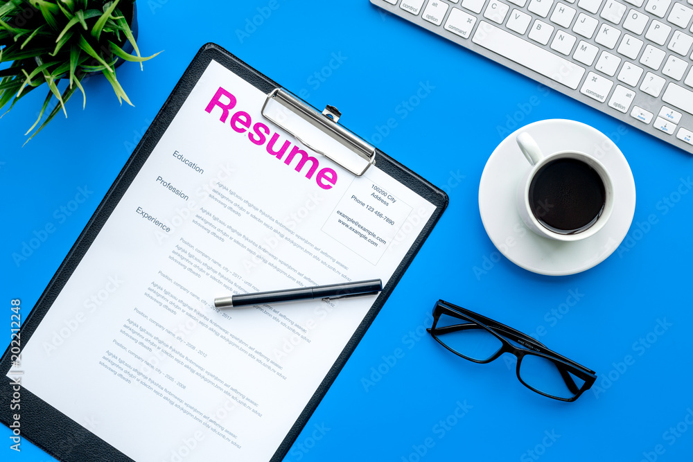 Empoyment concept. Resume on blue work desk with coffee, glasses, keyboard top view Empoyment concept. Resume on blue work desk with coffee, glasses, keyboard top view