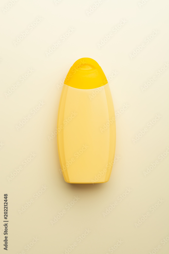 From above of yellow bottle for cosmetics or cream composed on beige surface. From above of yellow bottle for cosmetics or cream composed on beige surface.