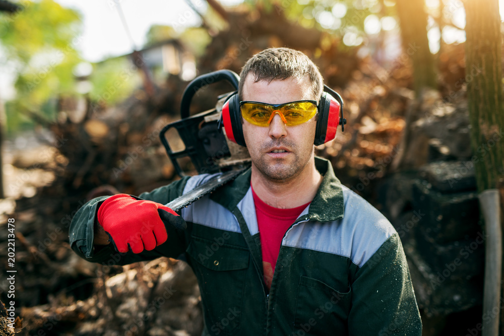 Close up of a professional lumberjack with eyeglasses and ear protection  holding a chainsaw on the shoulder while having a break. Stock Photo |  Adobe Stock