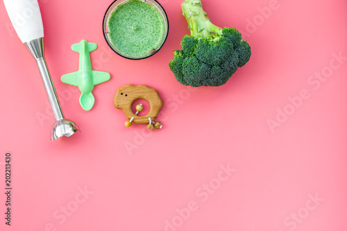 Homemade baby food. Cook puree with broccoli with immersion blender. Pink background with toy top view space for text