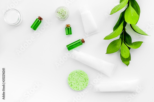Natural cosmetics for skin care near green leaves on white background top view copy space