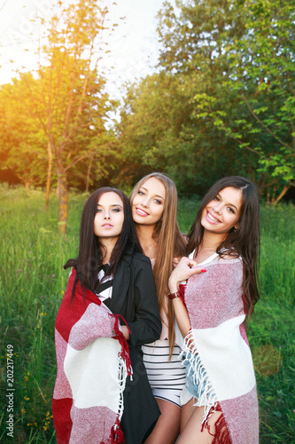 Three cute girls standing in the plaid outdoors, best friends having fun and laughing in park
