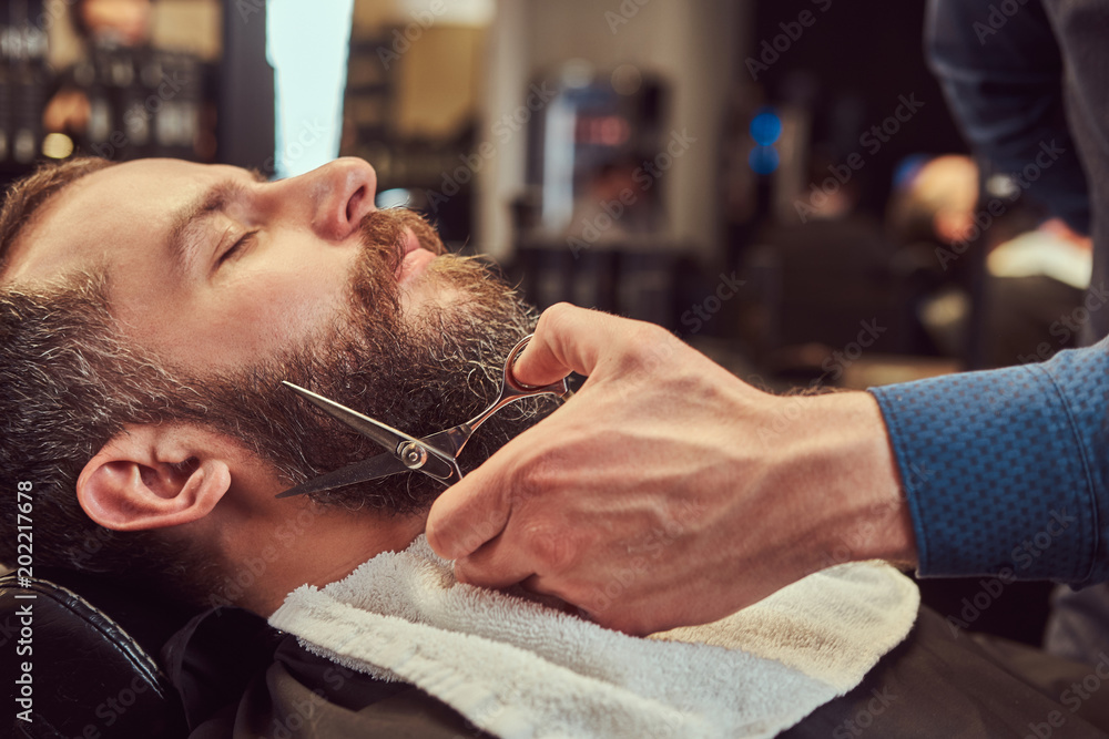 Fototapeta premium Profesjonalny model fryzjerski do modelowania brody z nożyczkami i grzebieniem w salonie fryzjerskim.