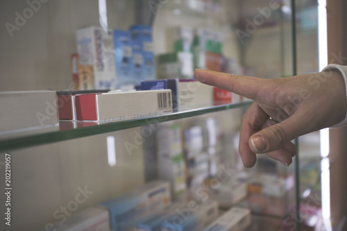Finger pointing to tablet against close up of shelves of drugs