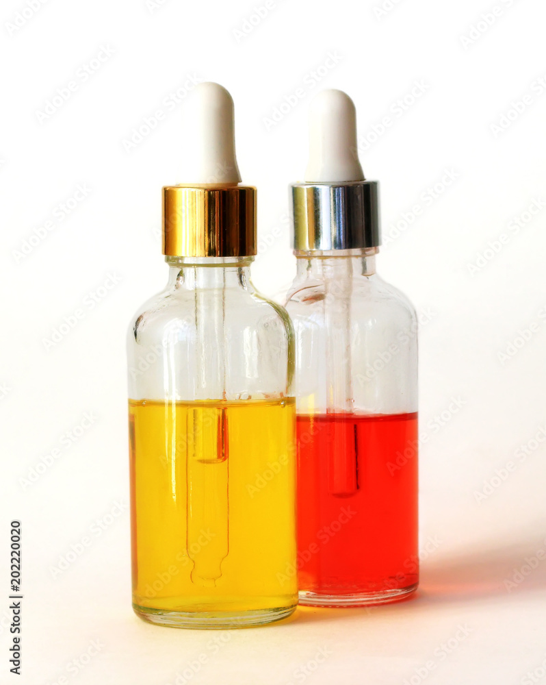  two glass clear bottles with pipettes and bright Golden and red cosmetic oils stands on white background