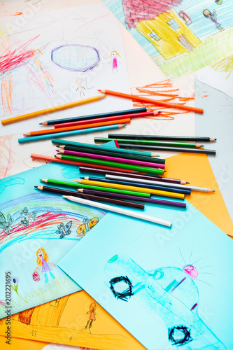 Pencil crayons scattered on desktop filled with colorful drawings