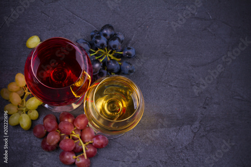 Red and white wine in wine glasses with grapes on dark stone background with copy space. overhead