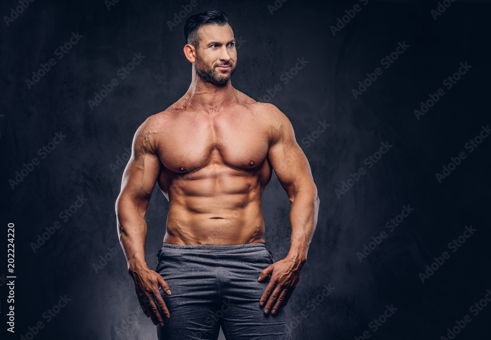 Portrait of a shirtless tall huge male with a muscular body with a stylish haircut and beard, in a sports shorts, standing in a studio.
