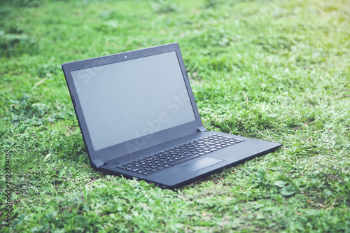 Black laptop with blank screen on grass.