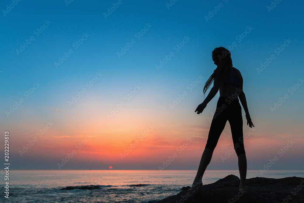 Silhouette flexible girl on the shore of Sea during twilight.