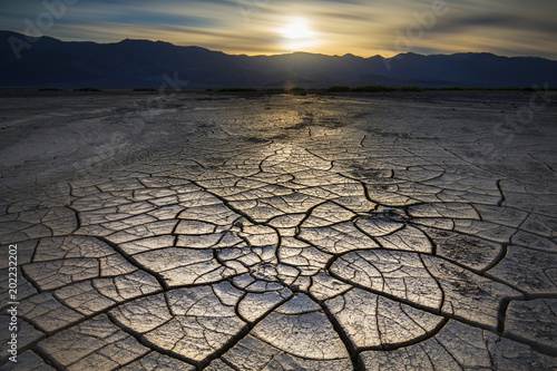 Big mud cracks light up in golden hour light with a sunset over the distant mountains