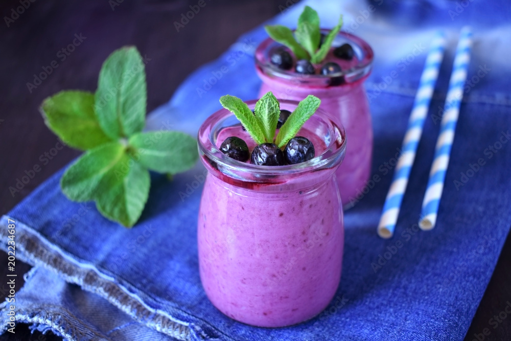 Blueberry smoothie in glass jars topped with berries and mint on blue background Blueberry smoothie in glass jars topped with berries and mint on blue background