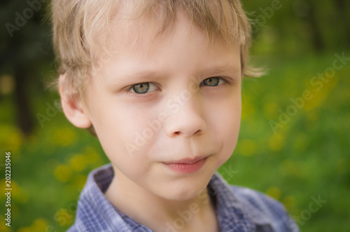 Closeup portrait of little cute funny boy with white hair looking at camera seriously while playing outdoors on warm spring or summer day. Horizontal color photography