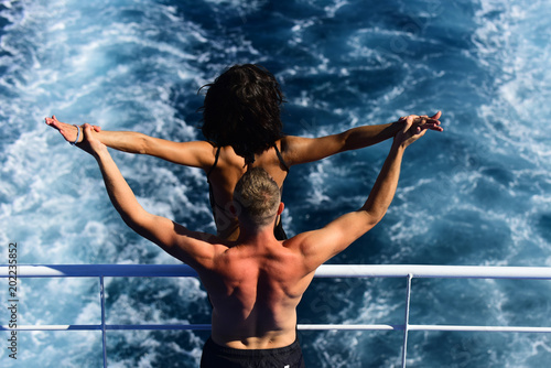 Attractive couple feel free and enjoy summer vacation. Freedom concept. Nude couple stands on deck of cruise liner with sea waves on background, rear view. Couple in love travelling on cruise ship. photo