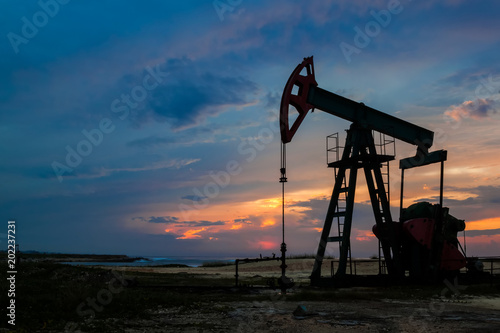 Silhouette of oil pump standing on the sea shore against the bright sunset sky background. Petroleum pollution concept.