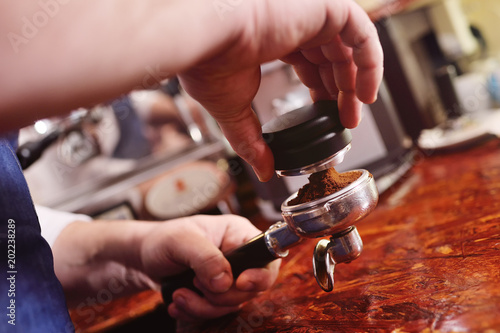 Holder with ground coffee and tamper for forming coffee pill close-up in the hands of barista