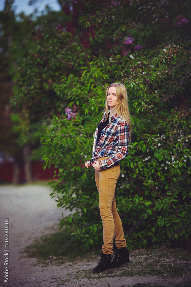 Fototapeta premium pretty woman blonde on a rustic road is happy, against a background of lots of green trees, a beautiful portrait of a rustic style, a simple home image